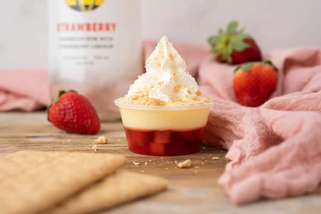 Strawberry jello shots with a cheesecake layer and whipped cream.