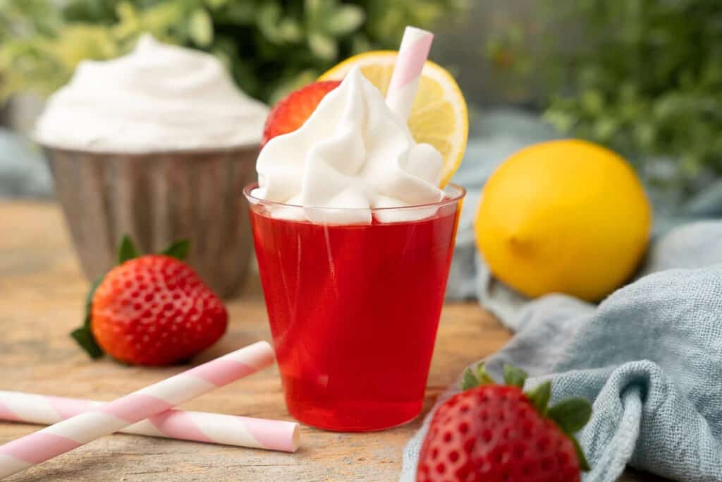 A strawberry jello shot with whipped cream on top.