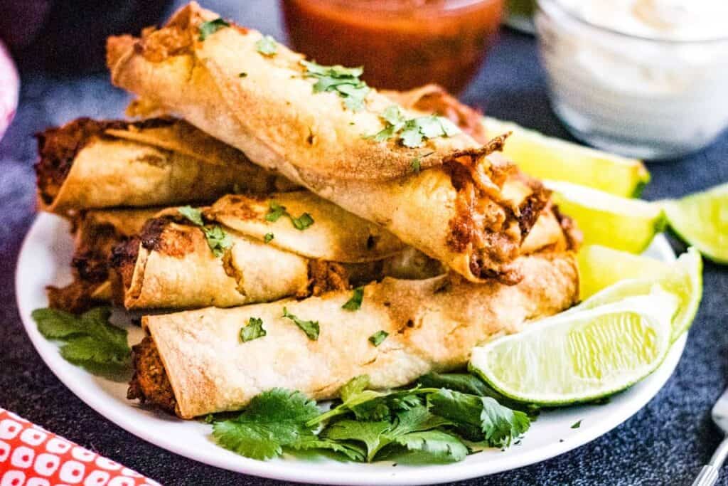 Air fryer chicken taquitos on a plate with a lime wedge and cilantro.