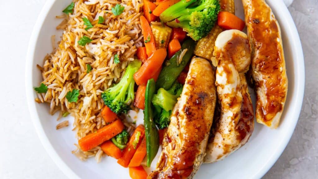 blackstone chicken tenders with rice and vegetables on a white plate.