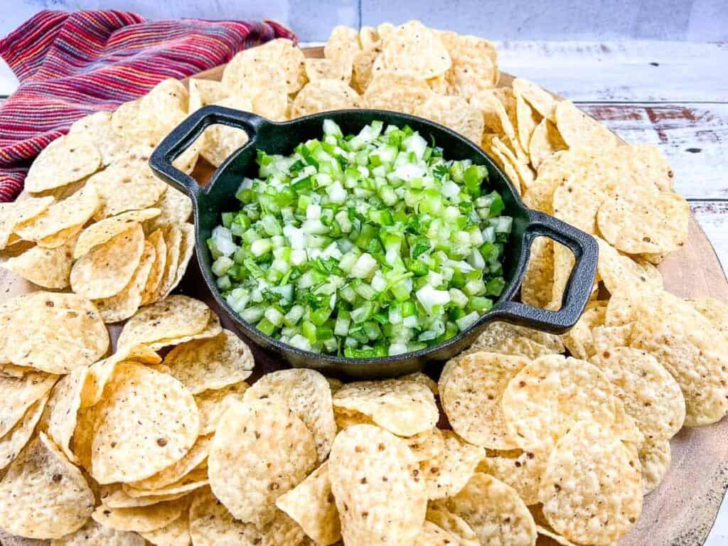 tomatilla pico de gallo in a cast iron container surrounded by tortilla chips.