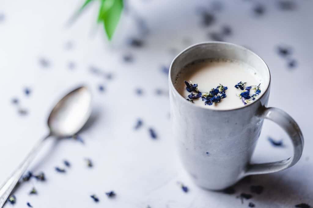 A white mug filled with a white liquid and garnished with purple flowers.