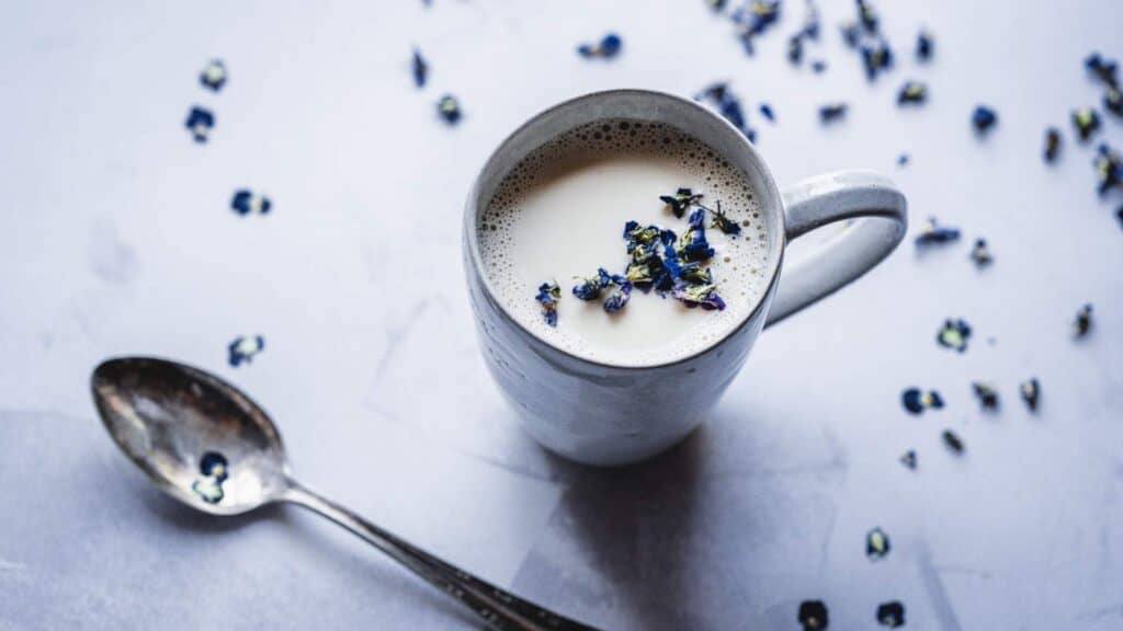 A white mug of white liquid scattered with purple flowers.