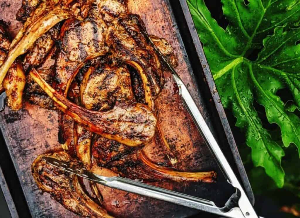 Grilled lamb chops piled onto a baking sheet.