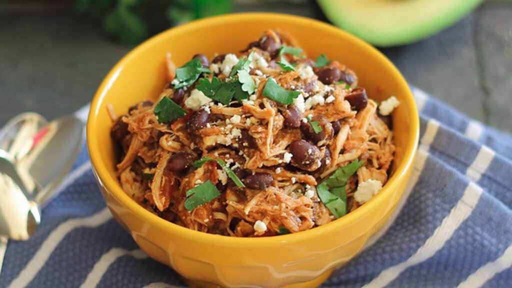 Four ingredient slow cooker pulled chicken with beans in a yellow bowl.
