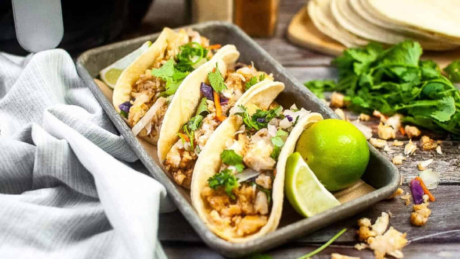 Fish tacos on a small baking sheet with limes.