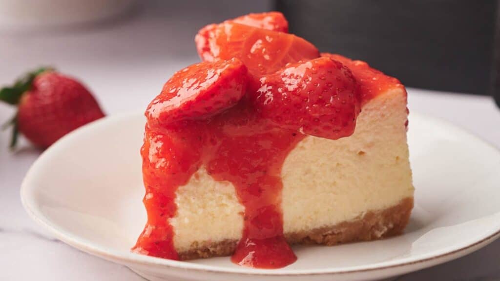 A slice of cheesecake on a plate with a delicious strawberry topping.