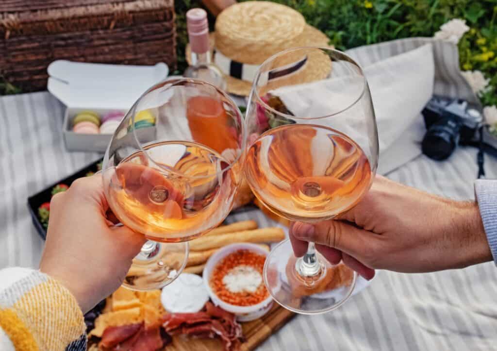 Two glasses of wine being held in hands above a picnic blanket.