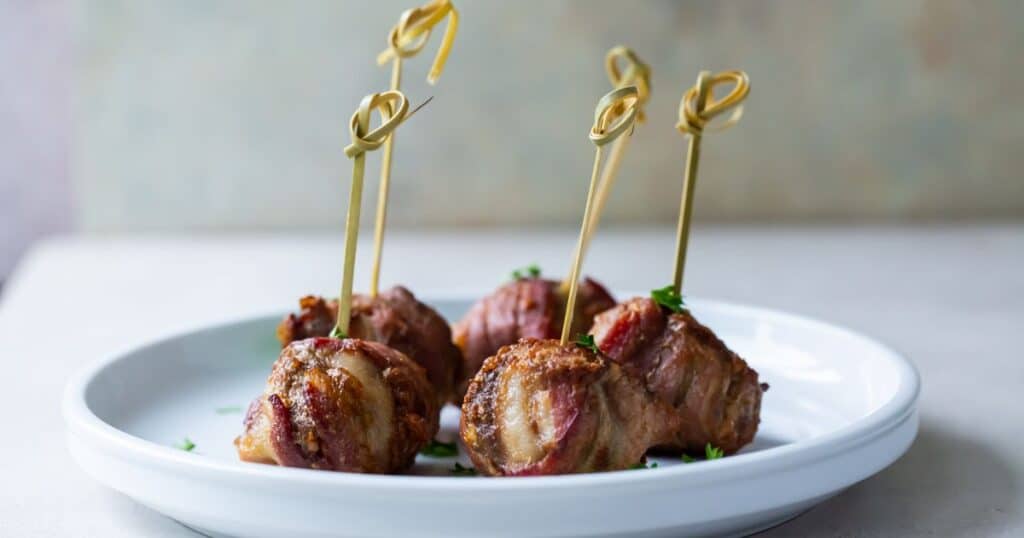 bacon wrapped keto meatballs with tooth picks on a white plate