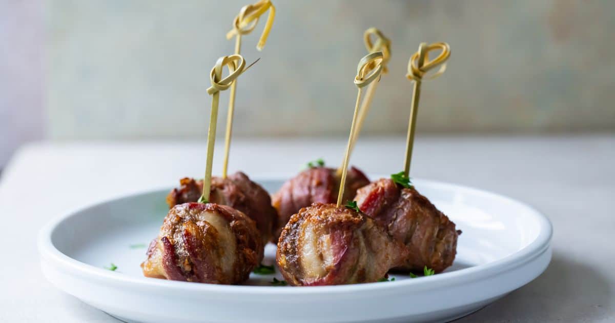 Air Fryer Bacon Wrapped Meatballs on a white plate with parsley and tooth picks.