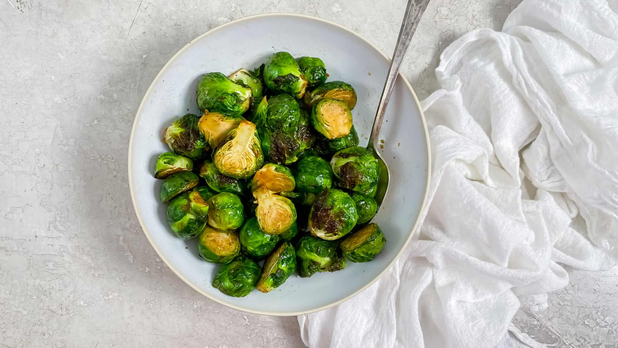 Air fryer Brussel Sprouts in a white bowl with a spoon.