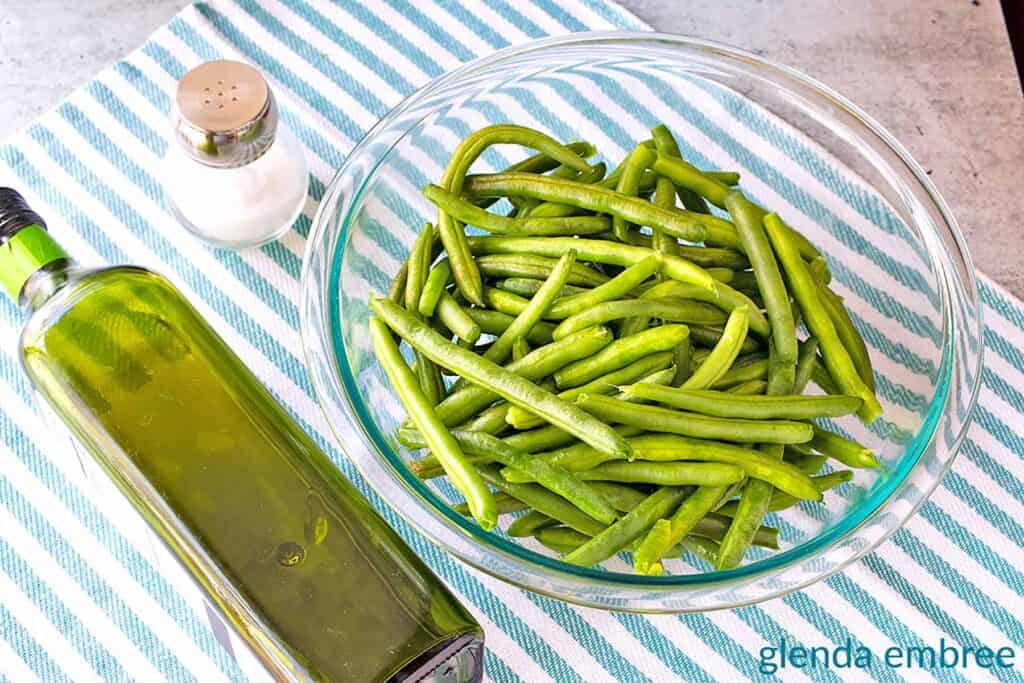 Green beans in a bowl next to avocado oil and salt.