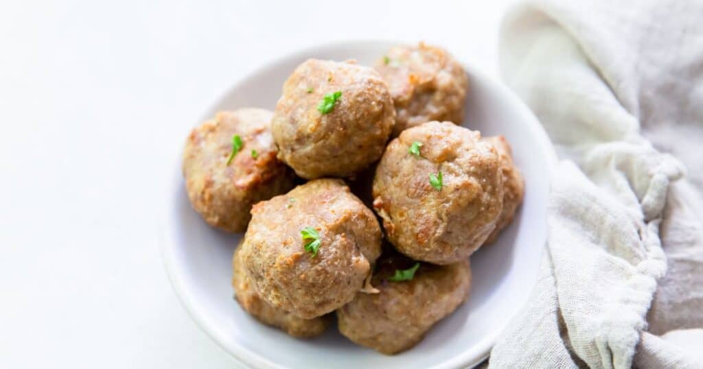 A bowl of low carb meatballs cooked in an air fryer, garnished with parsley on a white background.