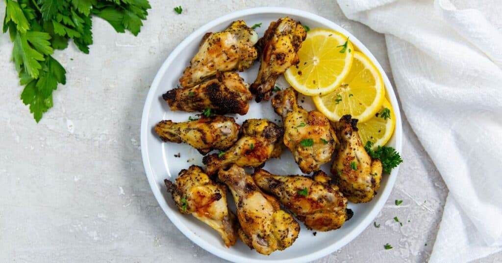 air fryer lemon pepper chicken wings on a white plate with lemons and parsley