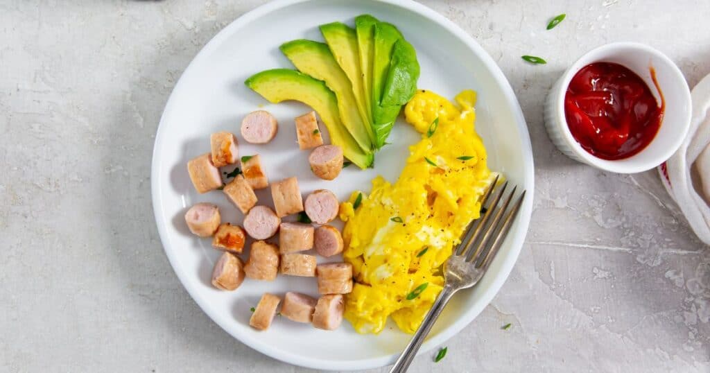 Trader Joe's breakfast chicken sausages cut up on a plate with eggs and avocado with a fork.