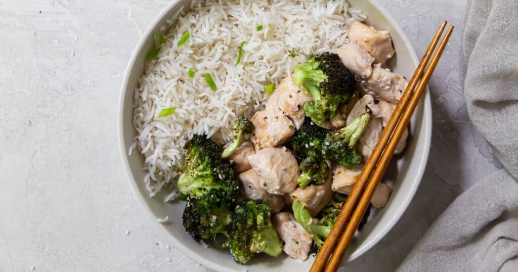air fryer chicken and broccoli in a bowl with rice and chop sticks.