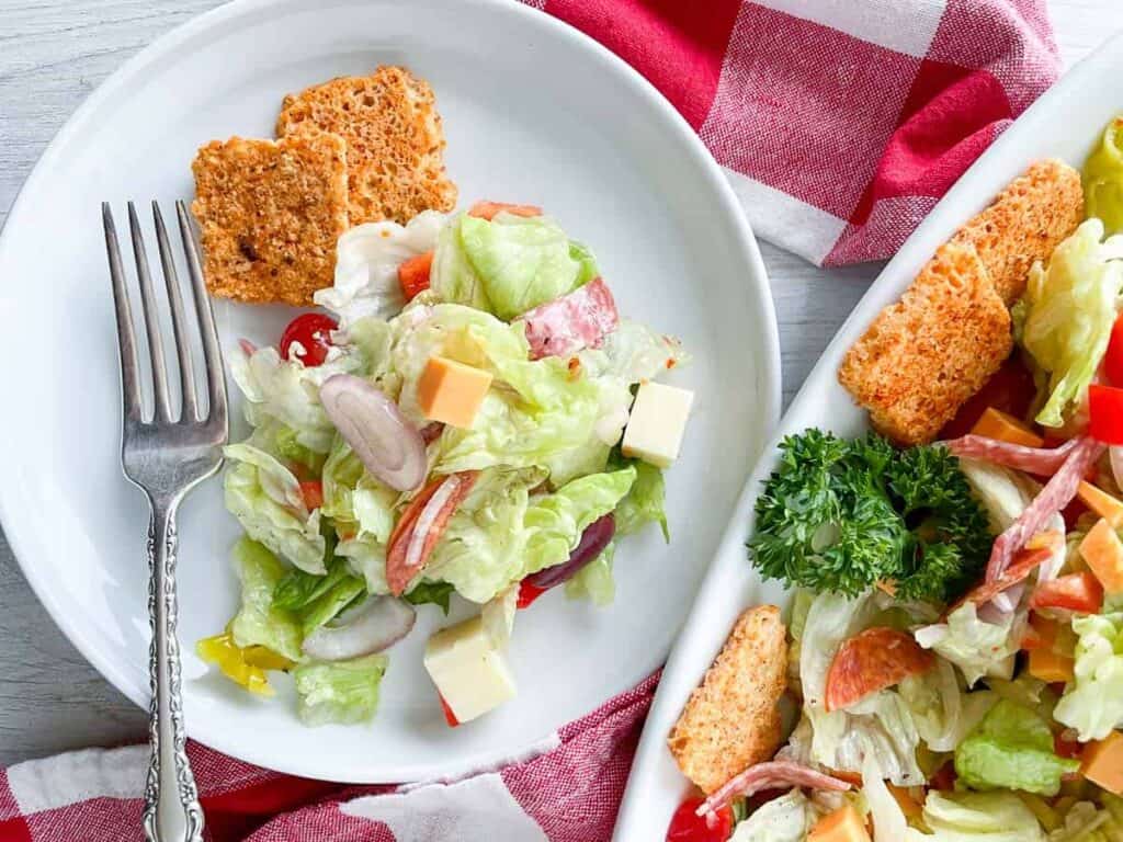 Antipasto salad on a plate with a fork and a checkered table cloth.