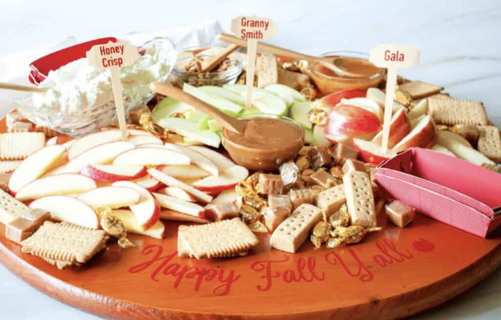 A tray of crackers, apples, and caramel on a wooden board.