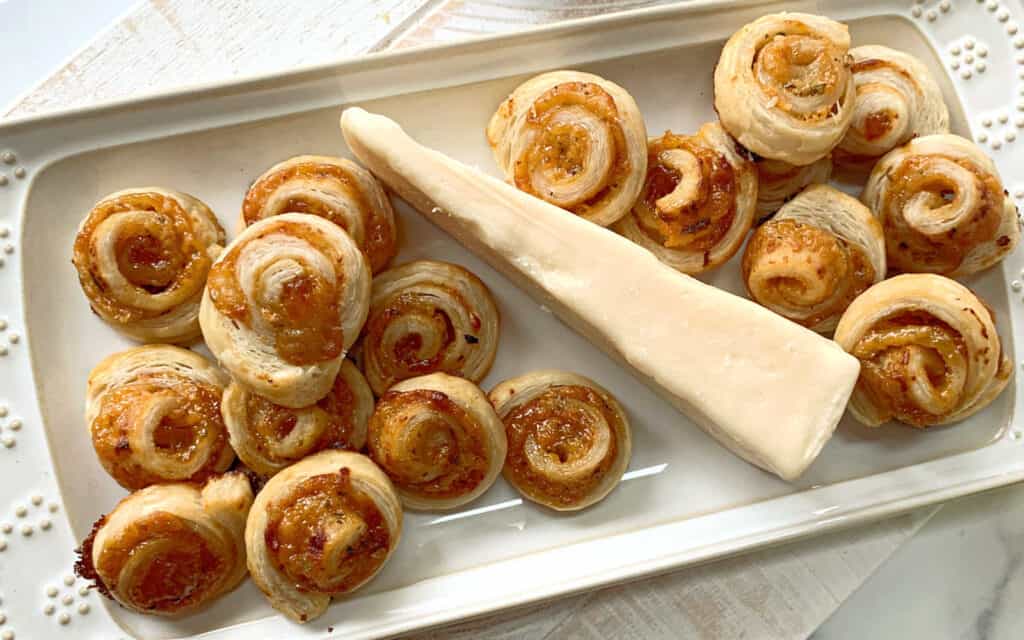 Apricot puff pastry pinwheels on a white trays with a wedge of cheese.