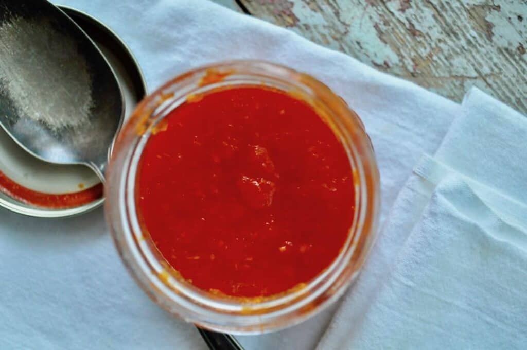 Top down view of homemade sriracha on a towel with a spoon next to it.