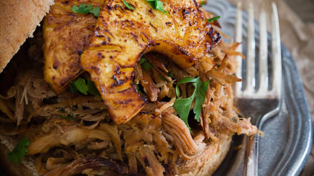 BBQ pulled pork sandwich with pickled pineapple slices.