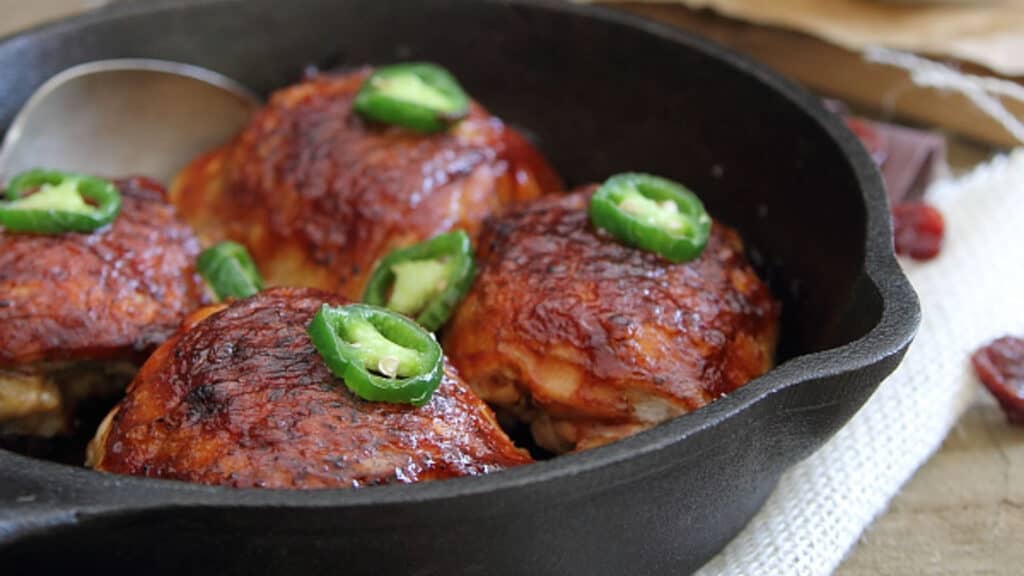 BBQ roasted chicken thighs in a cast iron skillet with jalapeño garnish.