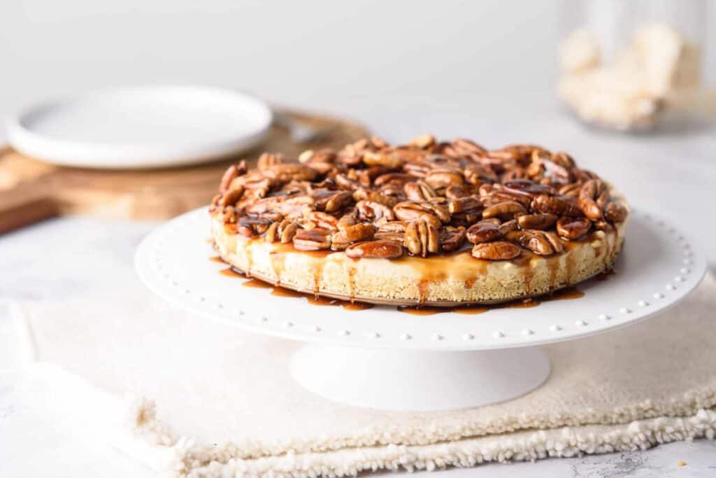 Pecan pie cheesecake on a white cake stand with a white napkin underneath.