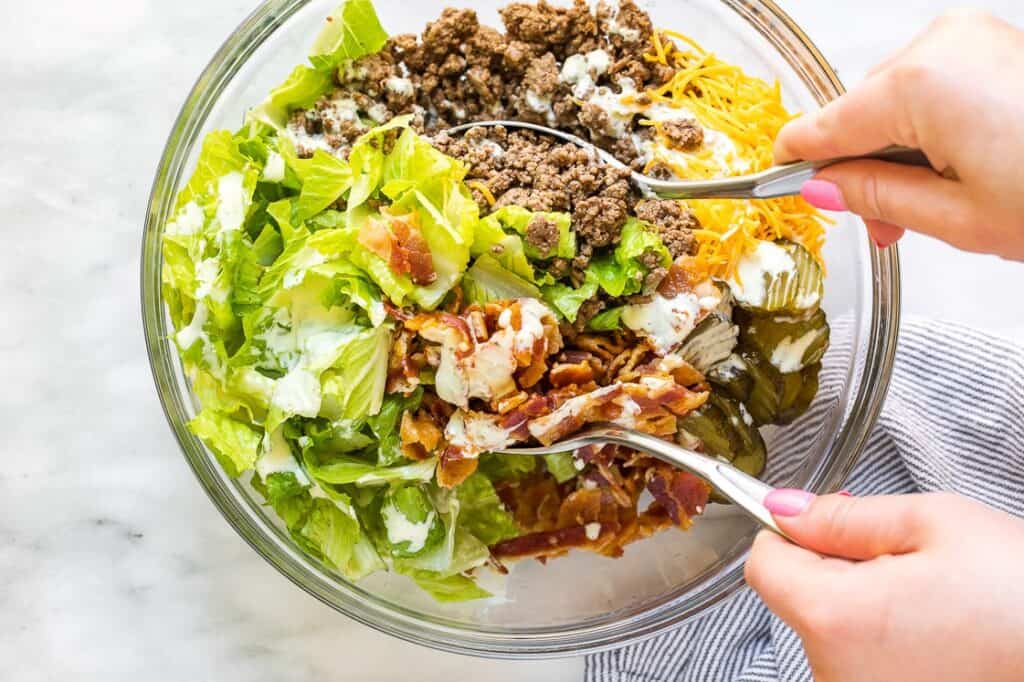 Hands scooping up a serving of bacon cheeseburger salad from a bowl.