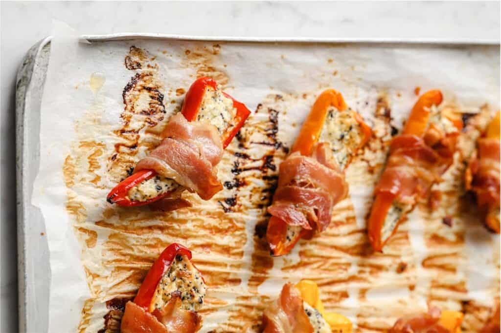 Baked bacon wrapped mini peppers on a baking sheet.