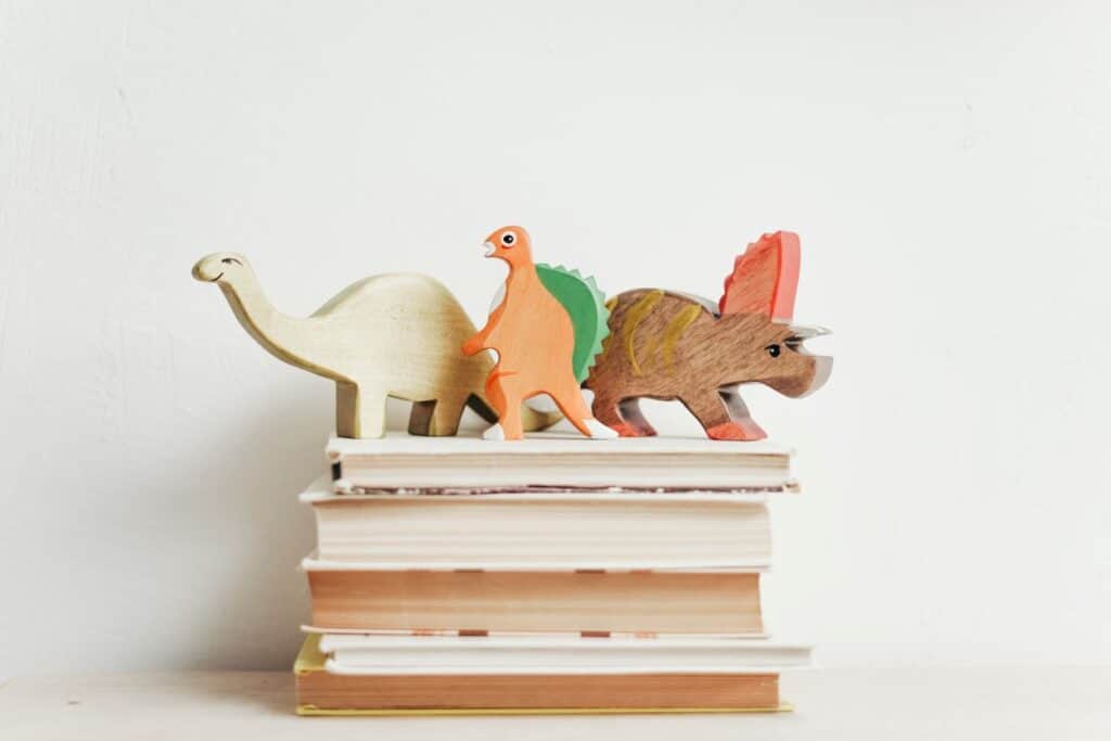 Books on shelf with wooden dinosaurs on top.