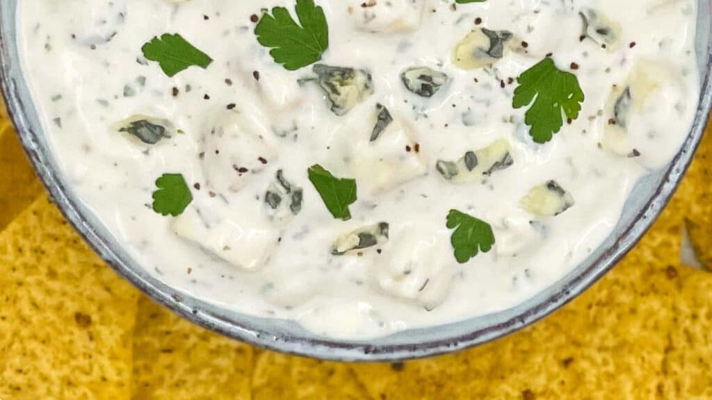 Blue cheese dressing in a serving bowl, you can see chunks of cheese and parsley.