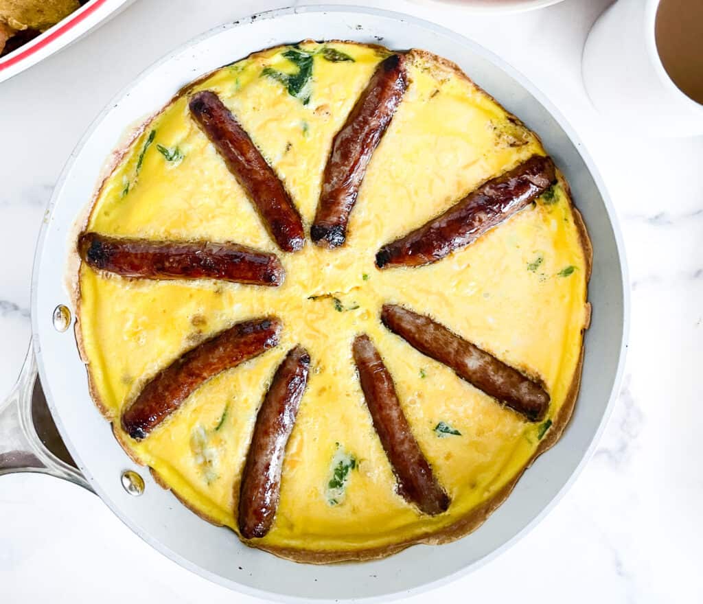 Overhead view of a finished sausage frittata in a white skillet.