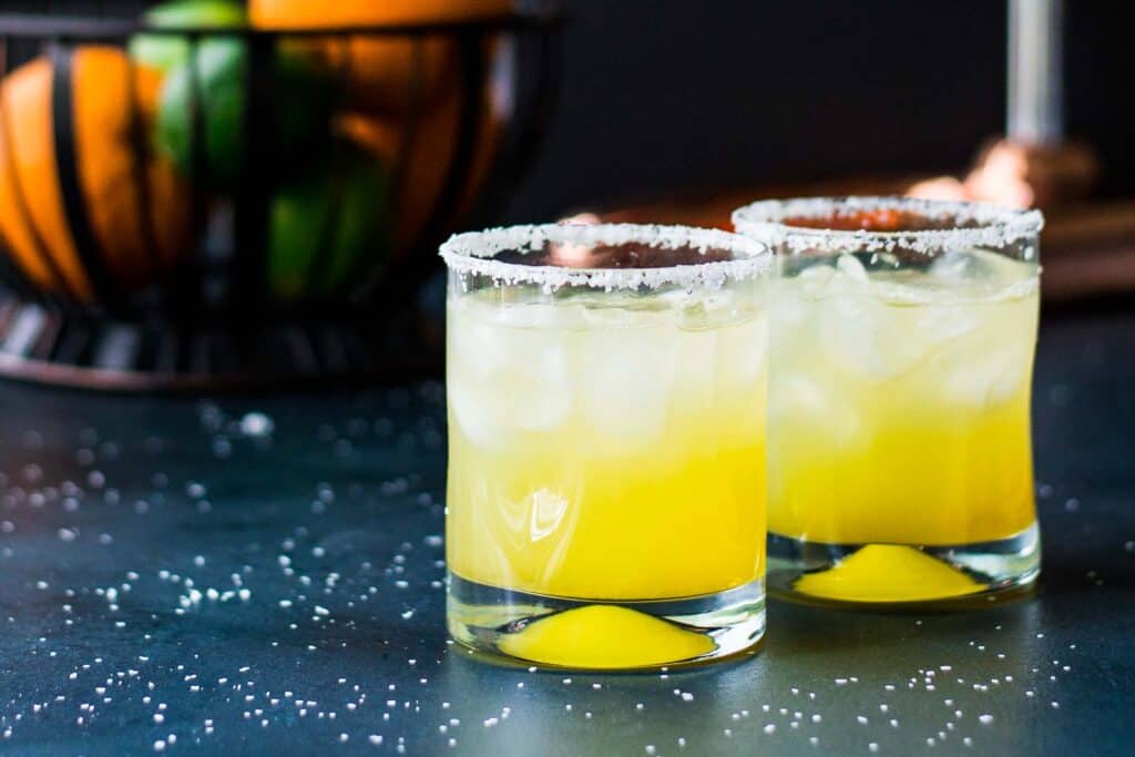 Two cadillac margaritas in front of a bowl of citrus fruit.