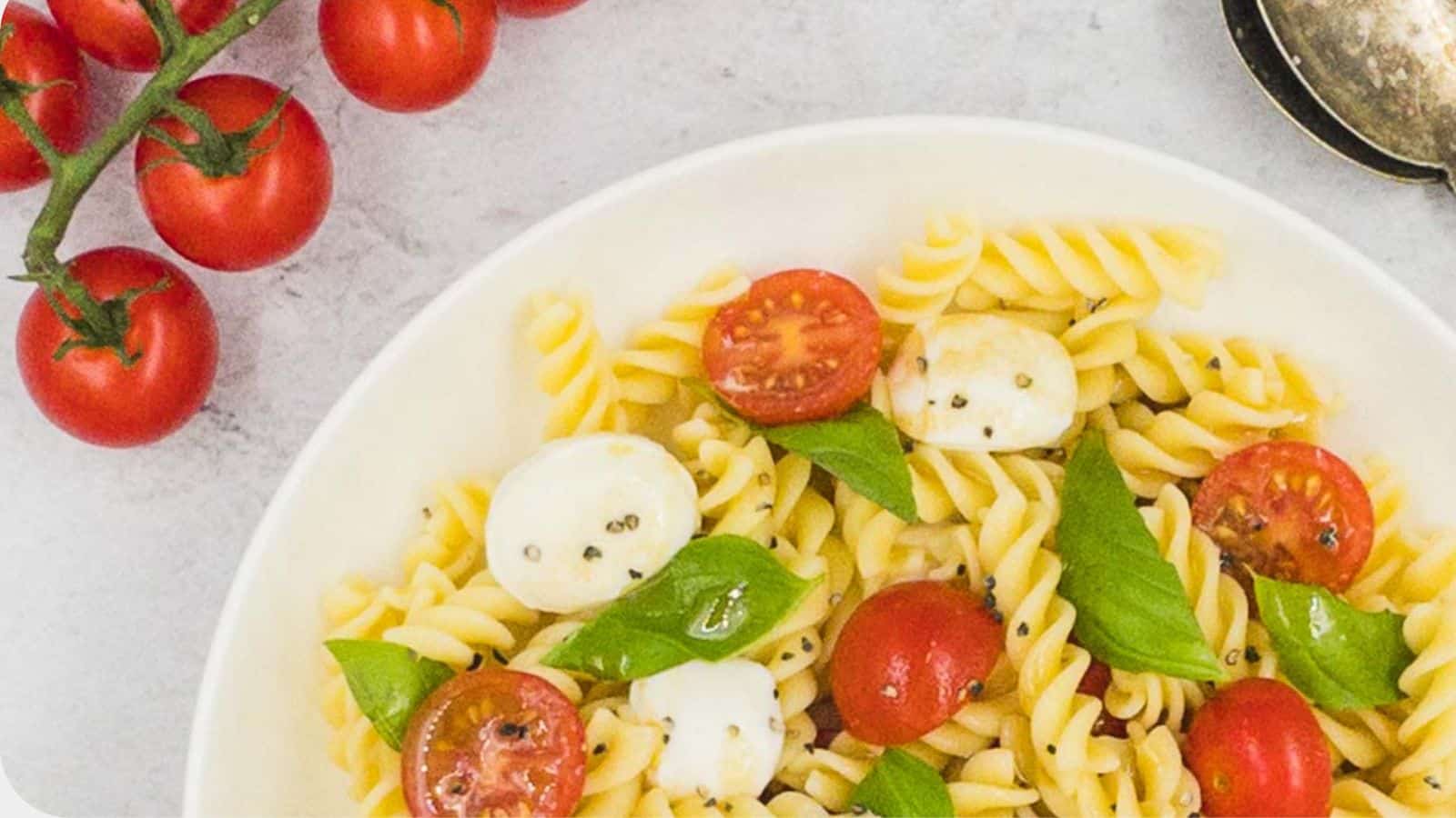 Caprese pasta salad in a bowl with fresh tomatoes by the side.