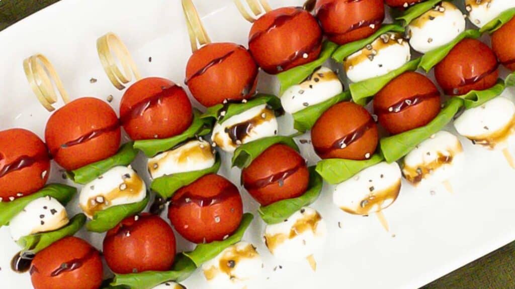 Caprese skewers on a serving dish with balsamic glaze drizzled over.