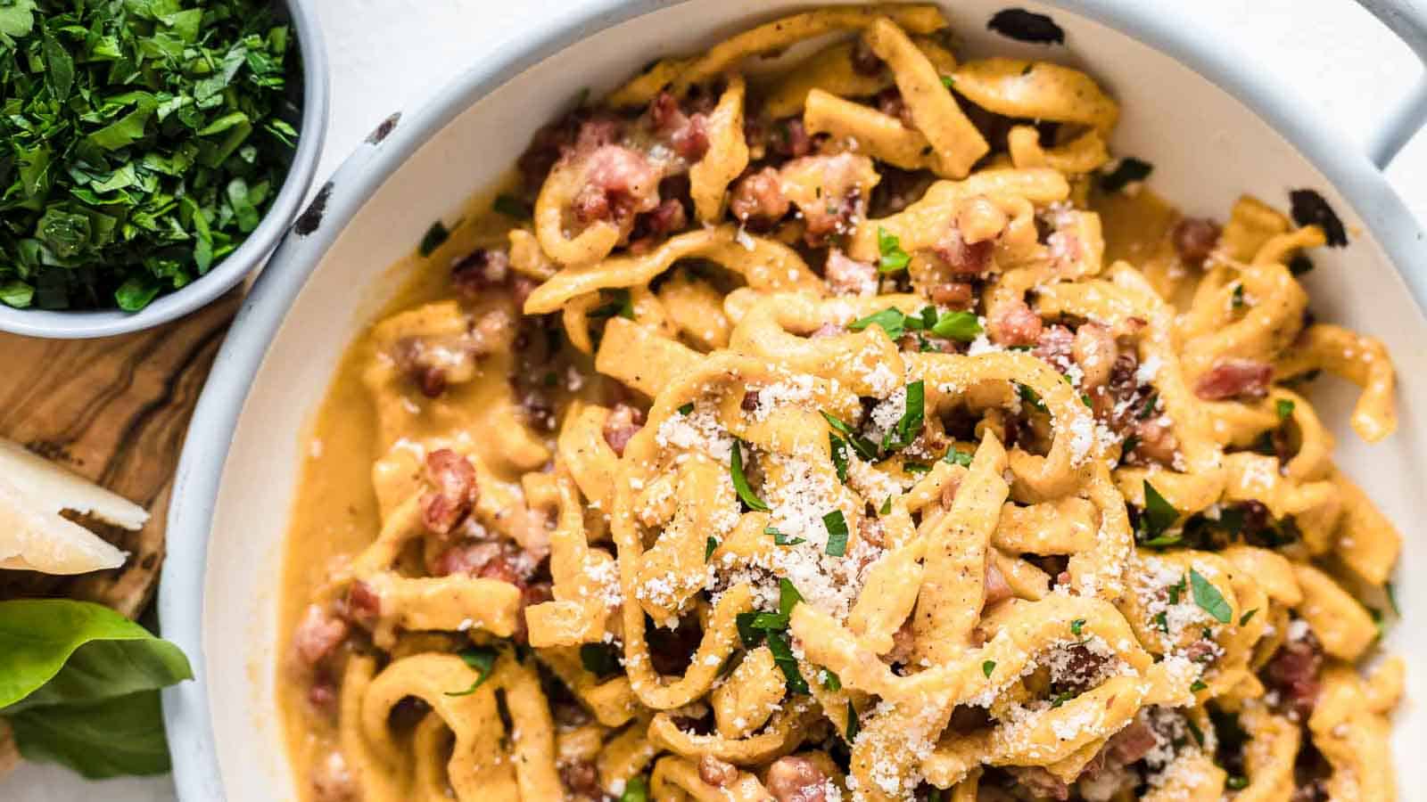 Pasta Carbonara inside a bowl with herbs and bacon.