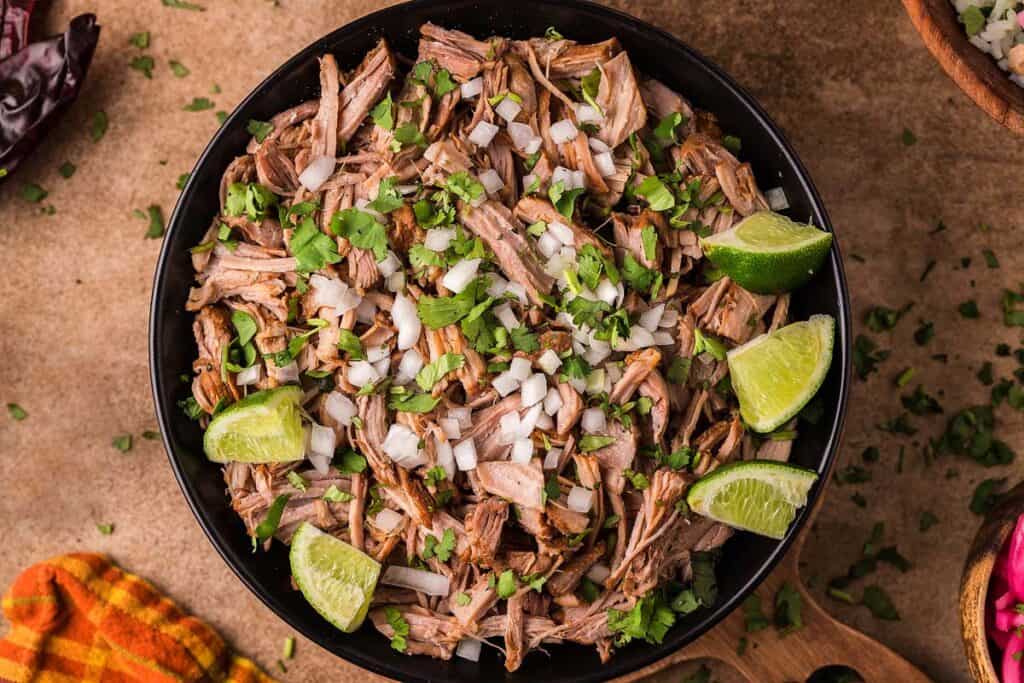 Pulled pork carnitas in a large black bowl on a table. 