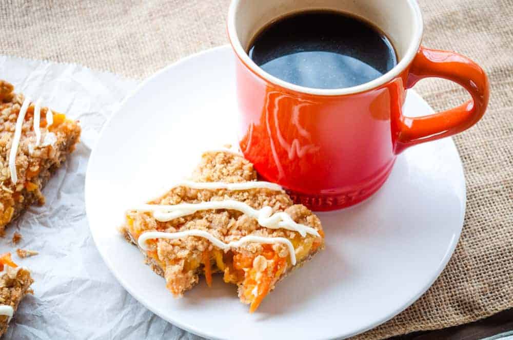 Carrot cake bar with a bite take out of it on a plate with a cup of coffee.