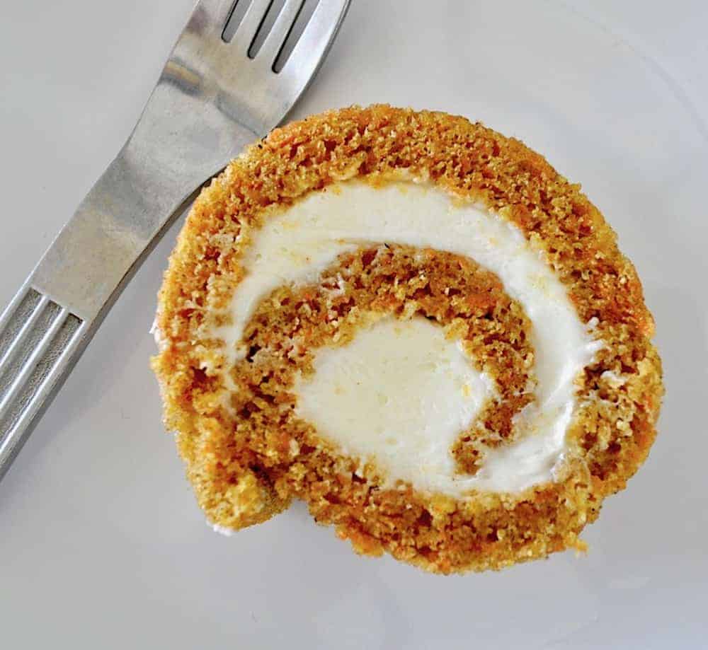 Slice of carrot cake roll on a plate with a fork.