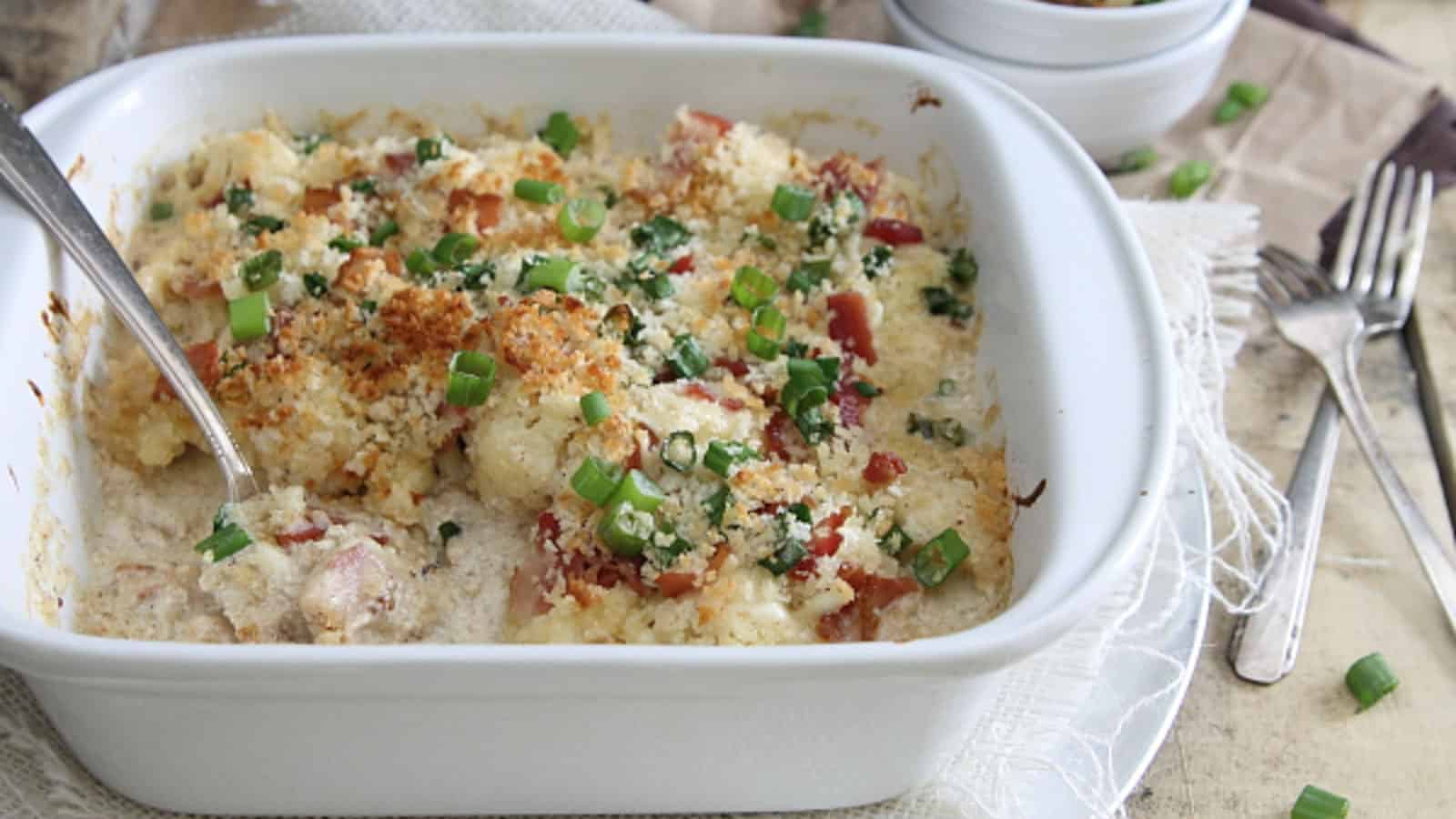 Cauliflower bacon gratin in a white baking dish with serving spoon.