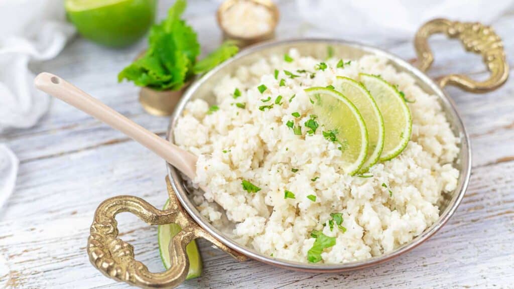 Coconut Cauliflower Rice inside golden plate with lime slices.