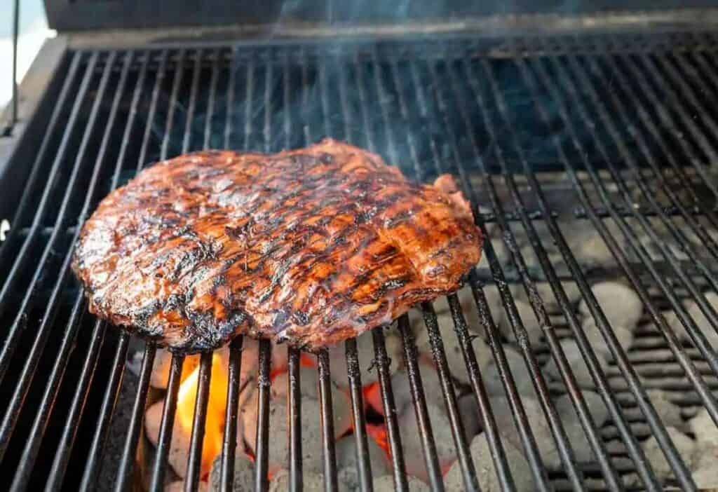 flank steak cooking on charcoal grill.