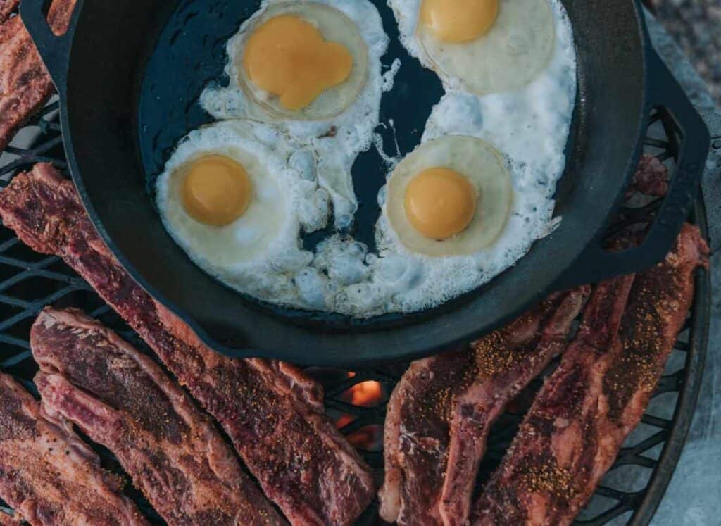 Short ribs on grill with skillet of eggs.