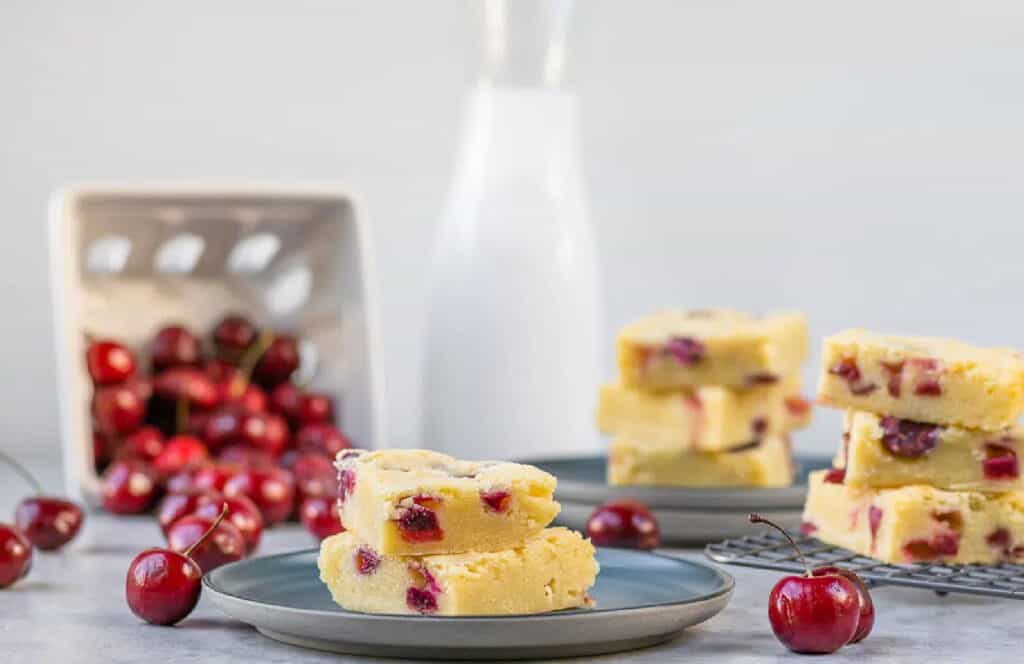 Cherry blondies on a blue plate with fresh cherries laying beside it.