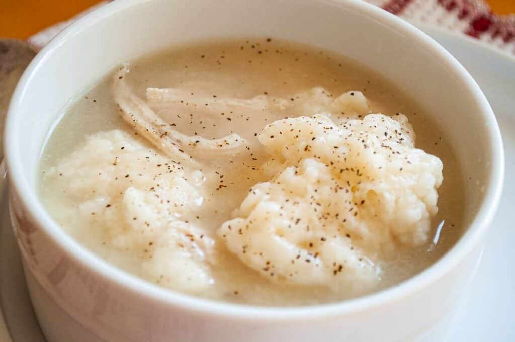 Chicken and dumplings in a bowl with a little black pepper on top.