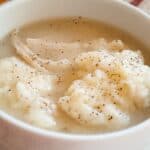 Chicken and dumplings in a bowl with a little black pepper on top.