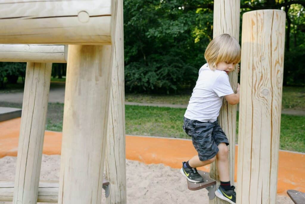 Child climbing on wooden playground equipment.