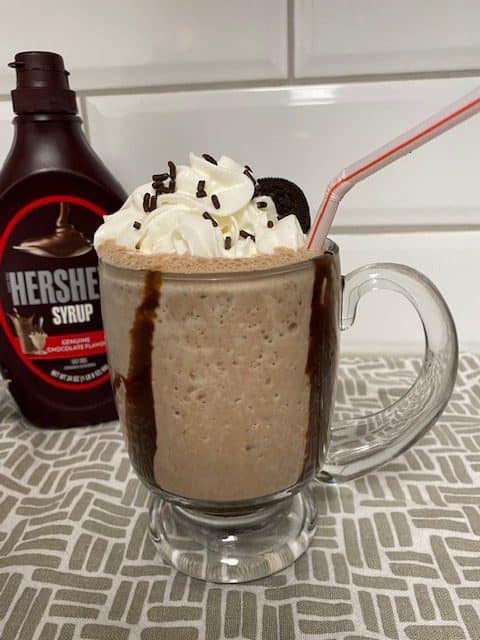 Chocolate Milkshake in a clear mug with shipped cream, sprinkles, and Oreo on top.