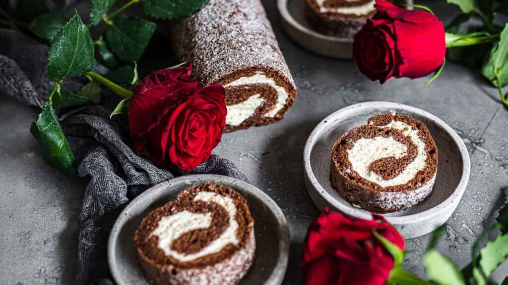 Low Carb Chocolate Roulade on a dark plates with roses around. 
