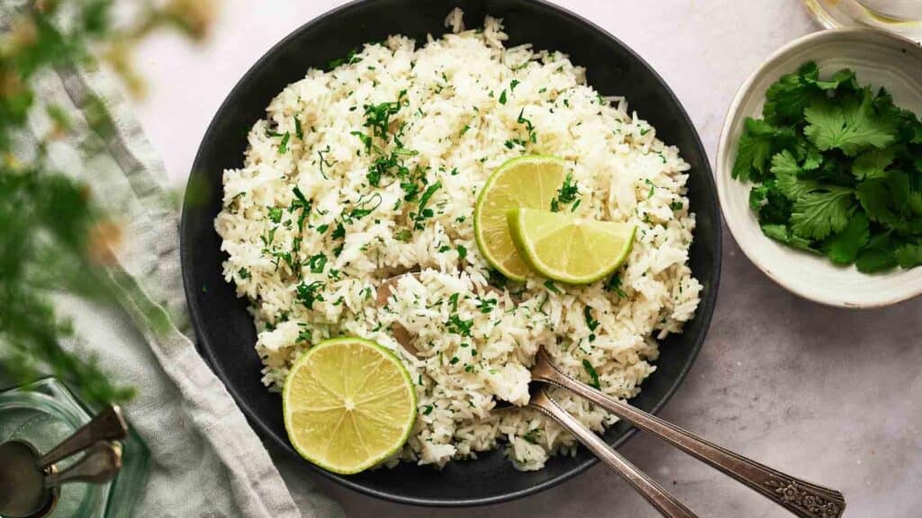 Chipotle rice in a bowl with sliced lime and spoons.
